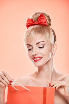 Beauty fashion portrait loving woman smiling looking into shopping bag. Confidence sensual attractive pretty nude blonde sexy girl, Pinup hairstyle, red bow.Unusual playful. Romantic, sale, discount