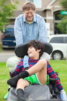 Father pushing ten year old  disabled son in wheelchair outdoors