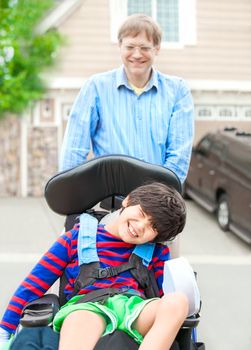 Father pushing ten year old  disabled son in wheelchair outdoors
