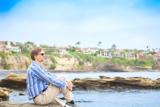 Caucasian man,  mid forties sitting  by rocky cliff near water