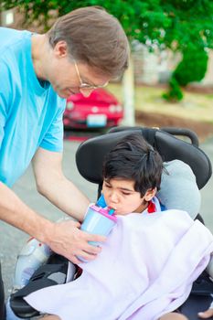Father helping disabled son in wheelchair drink from straw cup