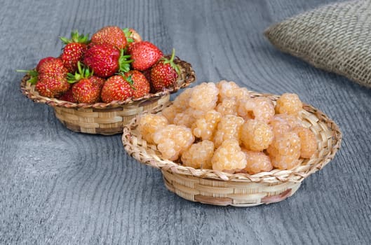 Raspberries and strawberries in wicker baskets, on wooden surface