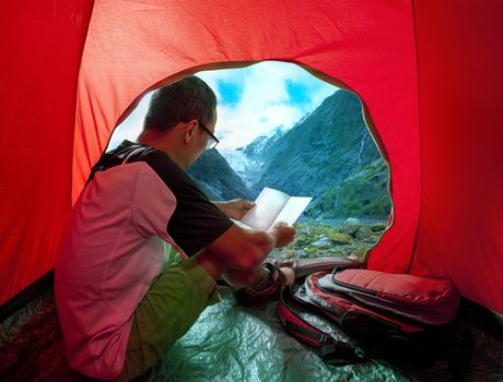 camping man reading traveling guide book in camp tent against be