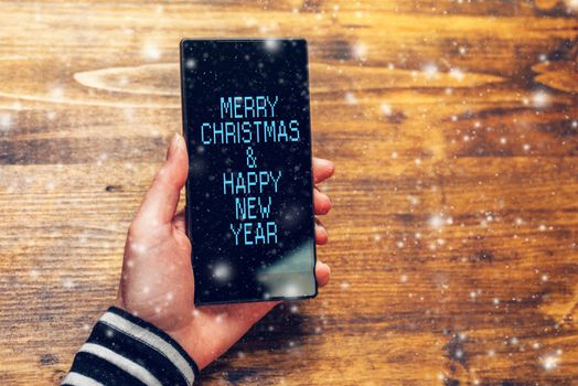 Merry Christmas and happy New Year message on mobile phone held by young adult caucasian female person