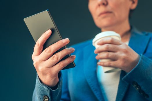 Satisfied businesswoman drinking coffee to go and looking mobile
