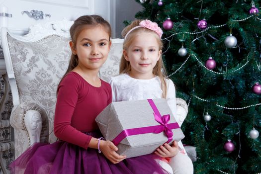 Two girls holding big gift-box under Christmas tree
