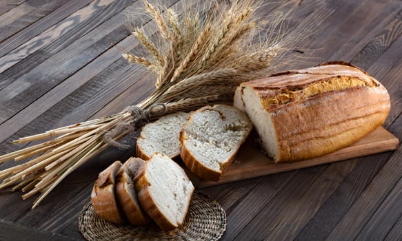 Slices of bread on a cutting board and ears of wheat on the wood