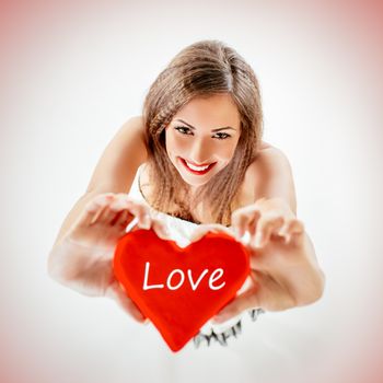 Beautiful smiling girl holding a red heart that says Love. Looking at camera. Selective focus.