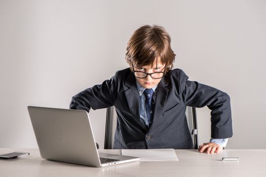 Schoolchild in business suit standing over desk