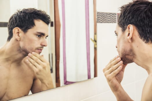 Shirtless young man examining his stubble in mirror