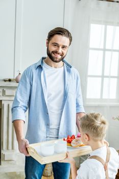 Smiling father and little son holding tray with tasty festive breakfast