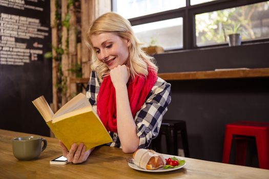 Young woman reading novel in cafeteria
