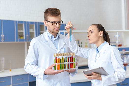 Professional chemists in white coats inspecting test tube with reagent in lab