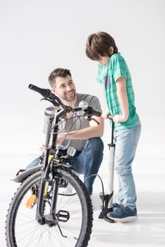 Happy father looking at son inflating bicycle tire with pump on 