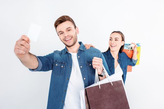 portrait of smiling couple holding shopping bags and credit card on white