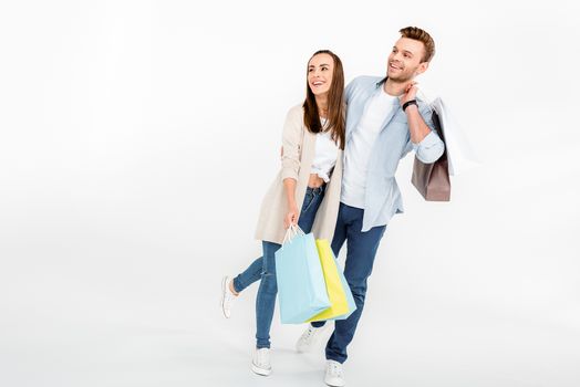 Happy young couple with shopping bags embracing and looking away on white 