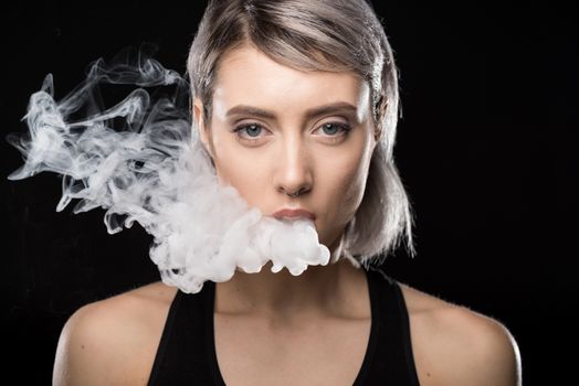 Attractive young woman vaping and blowing smoke on black