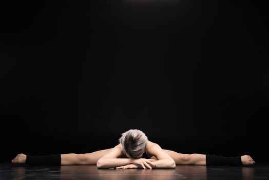 Young woman contemporary dancer stretching on black