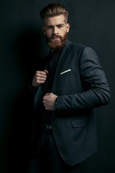 Stylish handsome bearded man in trendy suit posing on black
