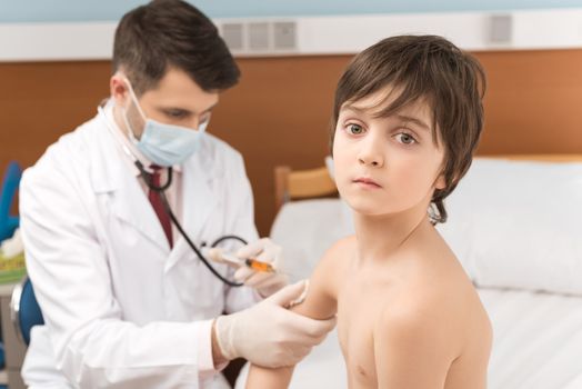 Man doctor examining shirtless child patient with stethoscope  