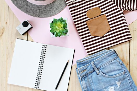 Lady's outfit with jeans short, blank notebook paper and action camera on wooden background, casual outfit for teenage girls
