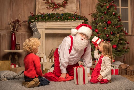 Happy Santa Claus and children sitting on carpet with Christmas gifts