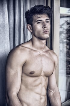 Sexy young man standing shirtless by curtains