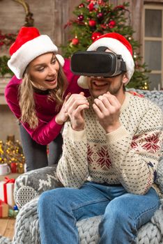 Happy couple in Santa hats using virtual reality headset 