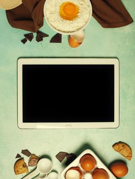 Baking background with ingredients for making chocolate chip cookies and tablet computer on blue rustic table. Top view. Flat lay style. Cooking meets technology