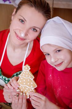 Mother and daughter holding Christmas tree biscuit made on kitchen