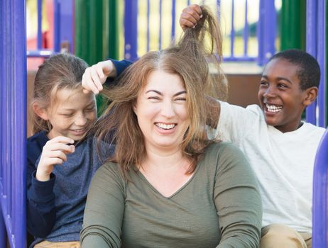 Laughing mother sitting with two sons playing with her hair