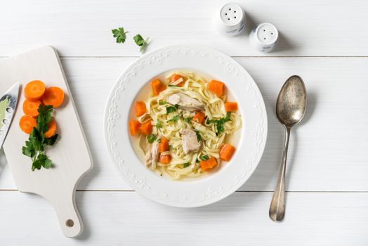 Top view of chicken soup with pasta, carrot and parsley on white