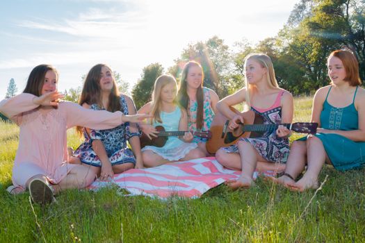 Girls Sitting Together in Grassy Field Singing and Playing Music