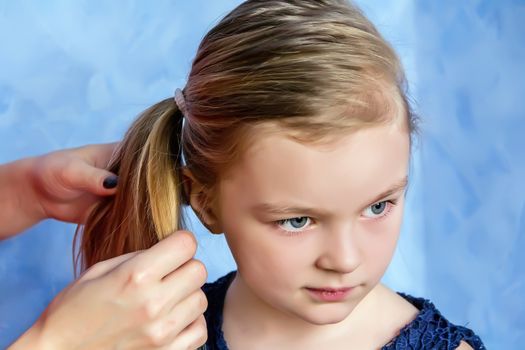 Mother makes hairstyle to daughter on blue