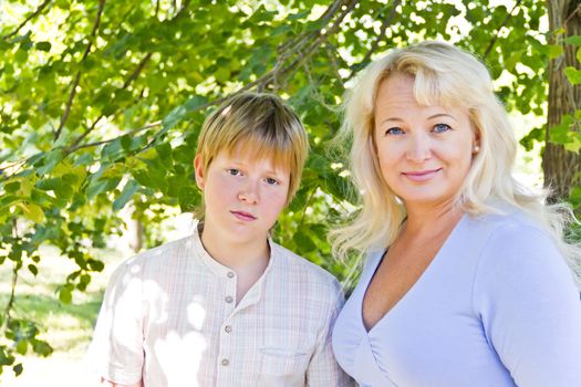 Blond woman and son smiling under green crone of tree in summer