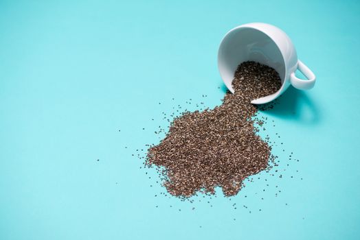 Nutritious chia seeds in cup on light blue background.