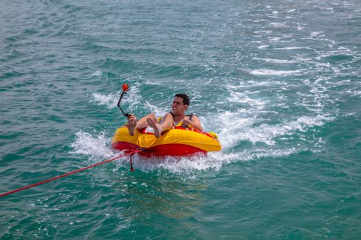 Man sitting in inflatable ring towed by a boat in the water and 