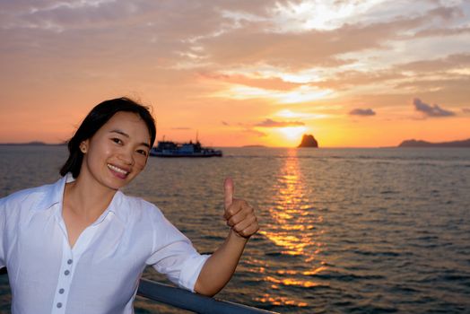 Women raise their thumb to admire the beautiful nature of colorful sky and sun at sunset over the sea on the deck of a passenger boat while cruising to Koh Samui Island in Surat Thani, Thailand
