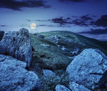 mountain summer landscape. meadow with huge stones among the grass on top of the hillside near the peak of mountain range at night in full moon light