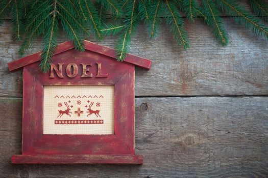 Noel house shaped frame with branches of Christmas-tree on old wooden background