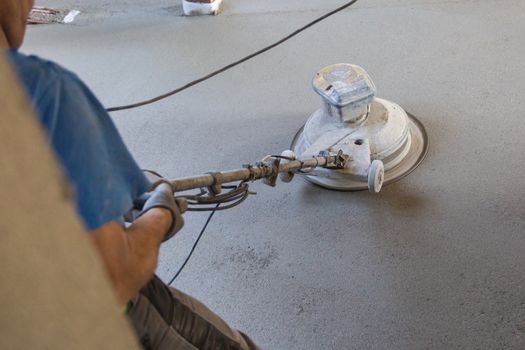 Laborer polishing sand and cement screed floor.