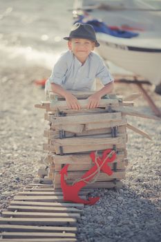 Handsome Nice looking boy on beach walking posing on wooden way wearing fancy stylish blue shirt and shorts with gallows and gentleman hat enjoy summer time alone on awesome ocean with anchor