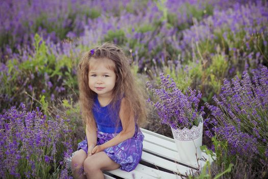 Pretty young girl sitting in lavender field in nice hat boater with purple flower on it.