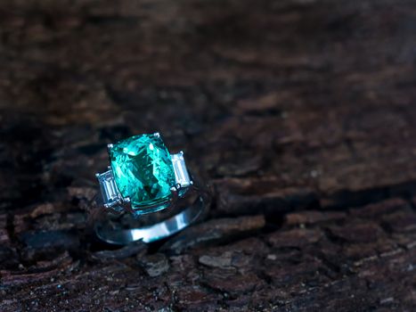 Closeup green gem ring with white diamond on old wooden backgrou