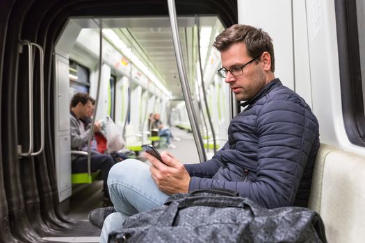 Male commuter reading from mobile phone screen in metro.