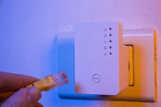 Man insert ethernet cable into WiFi extender device which is in 