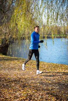 Young Sports Man Running in the Park in Cold Sunny Autumn Morning. Healthy Lifestyle and Sport Concept.