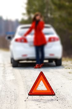 Woman standing by the broken car and warning triangle sign