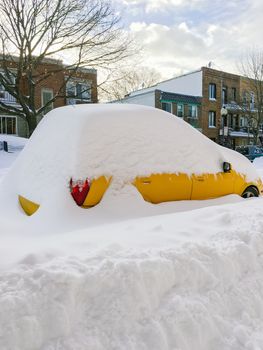 Urban street with a yellow car stuck in snow. Montreal, Quebec, Canada.