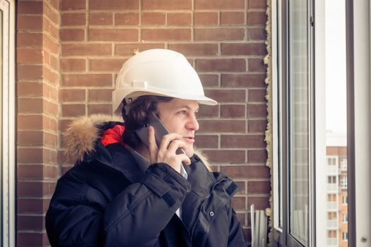 Young civil engineer is having trouble over the phone against brick background. Soft focus, toned